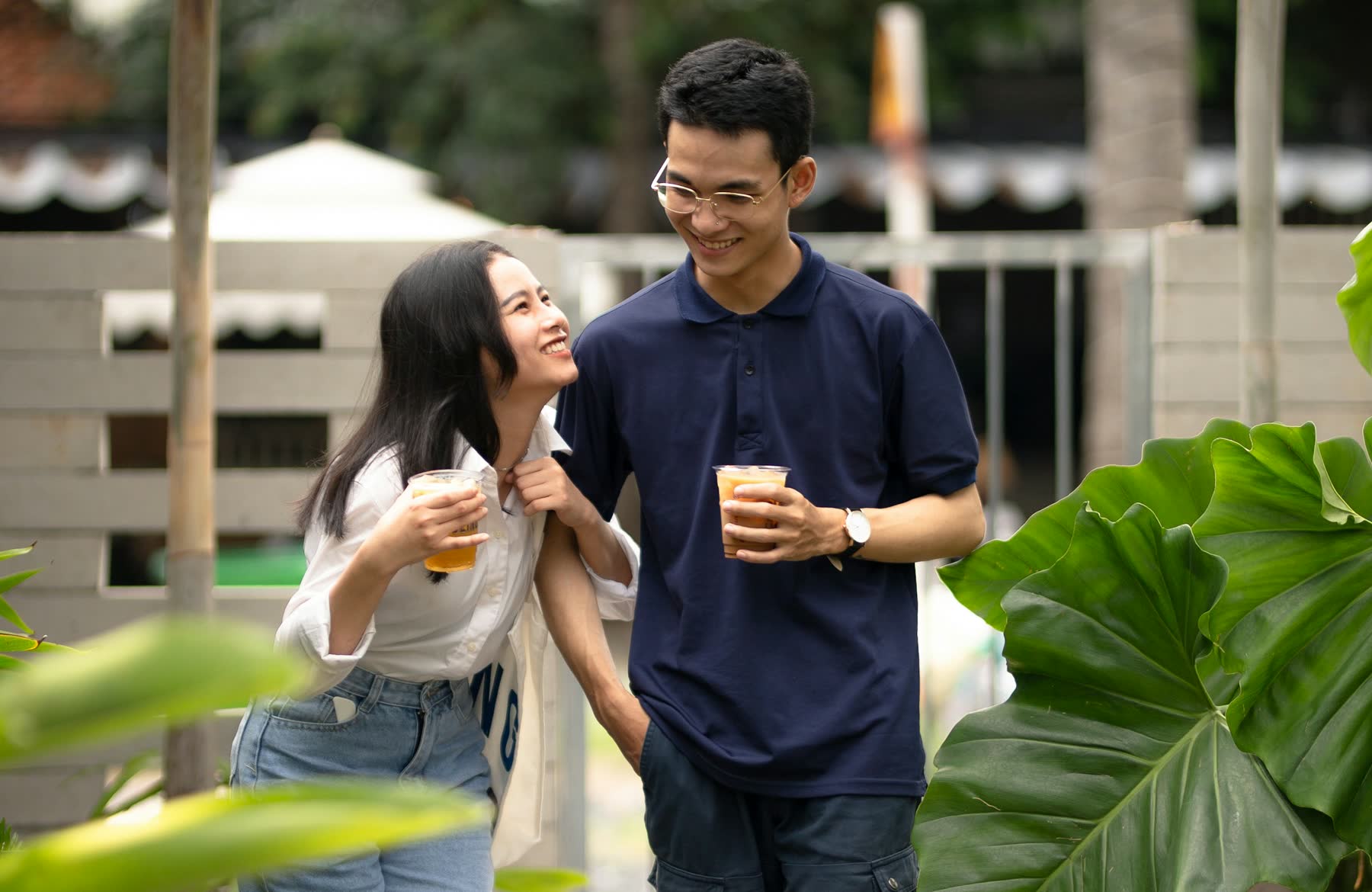 A man and a woman walking together with takeaway coffees, mid-conversation