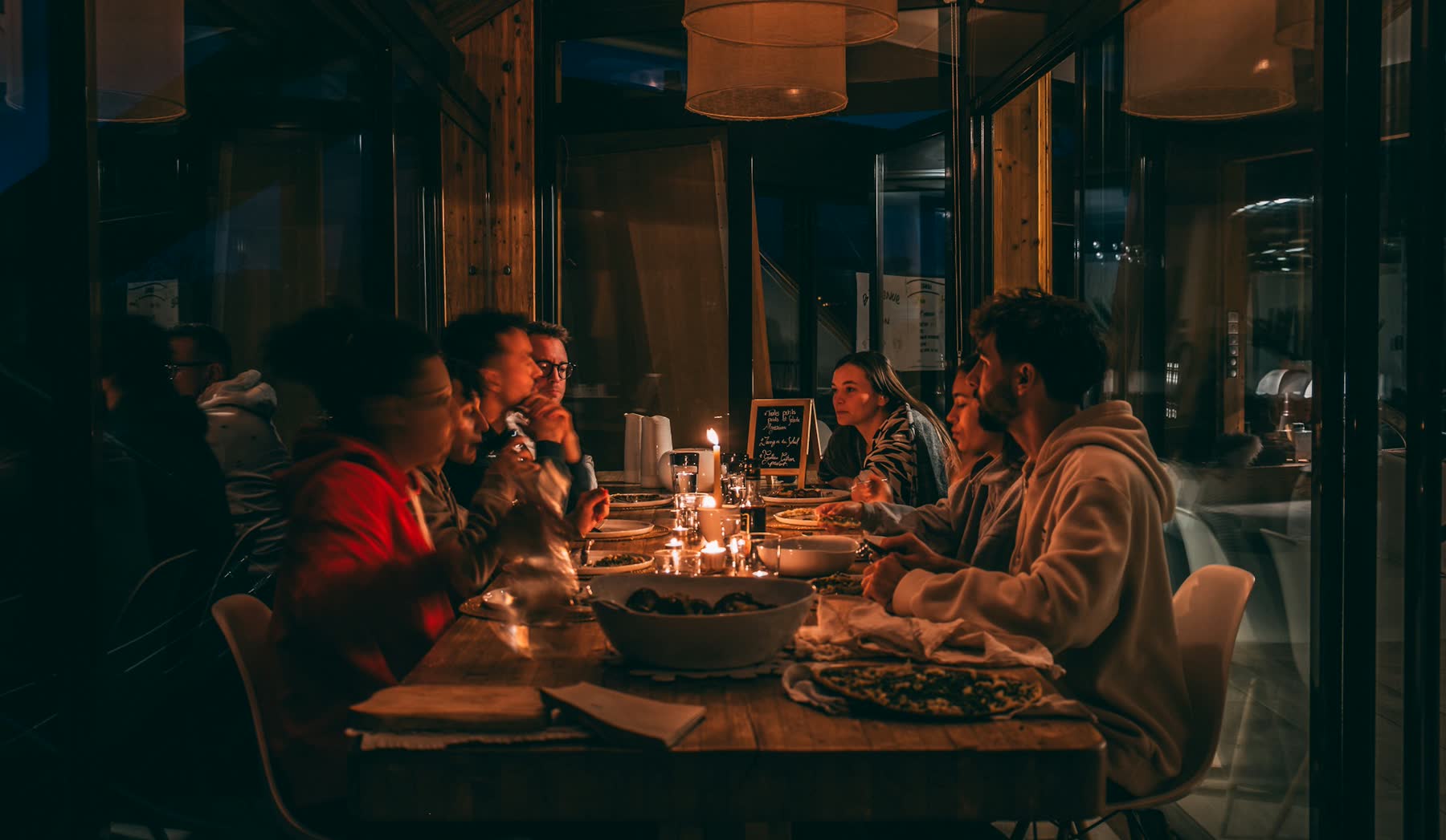 Friends around a candlelit table at a warm, dimly lit restaurant, sharing plates
