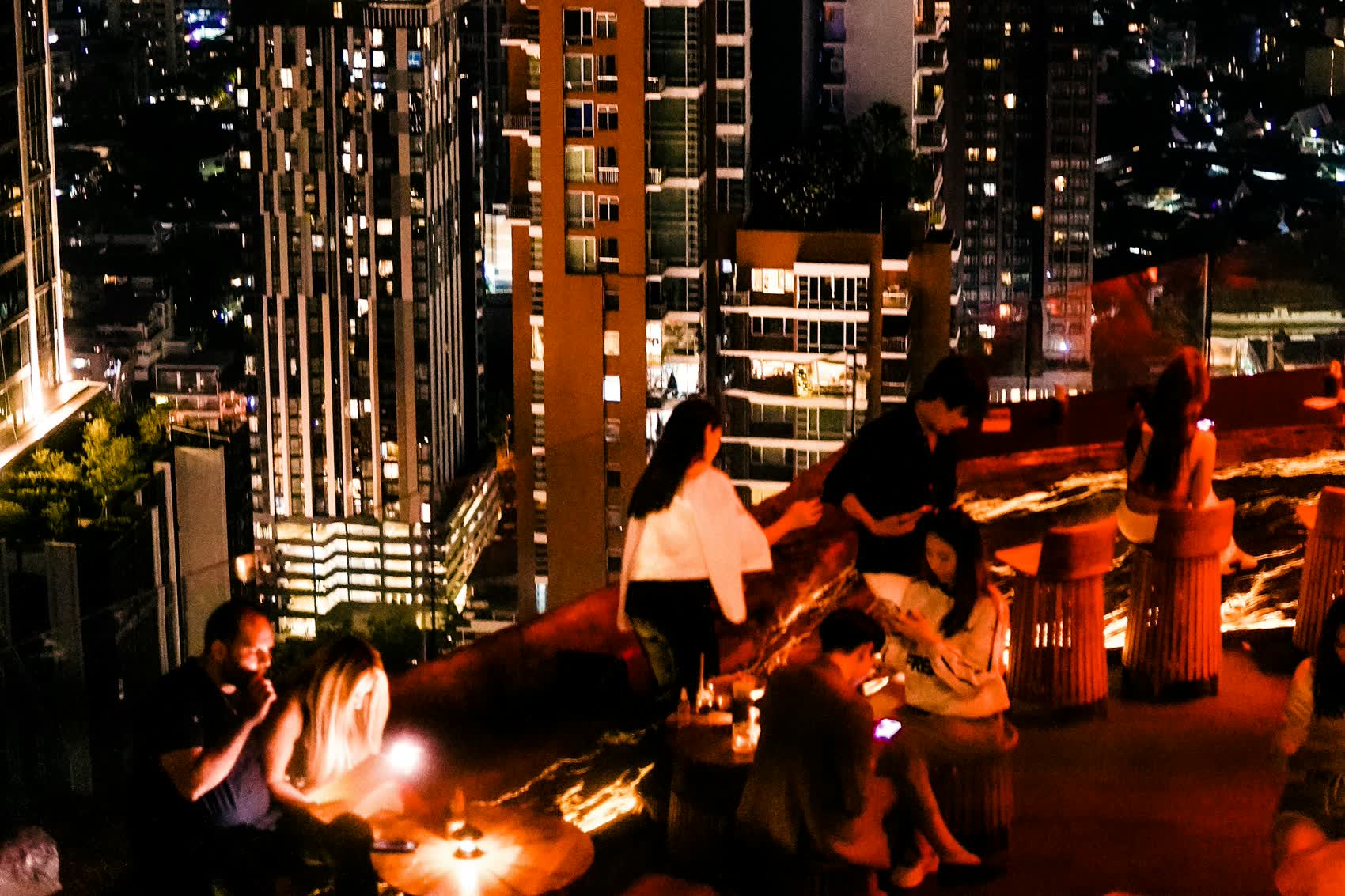 An upscale rooftop bar at night, people with cocktails above a city lit up below